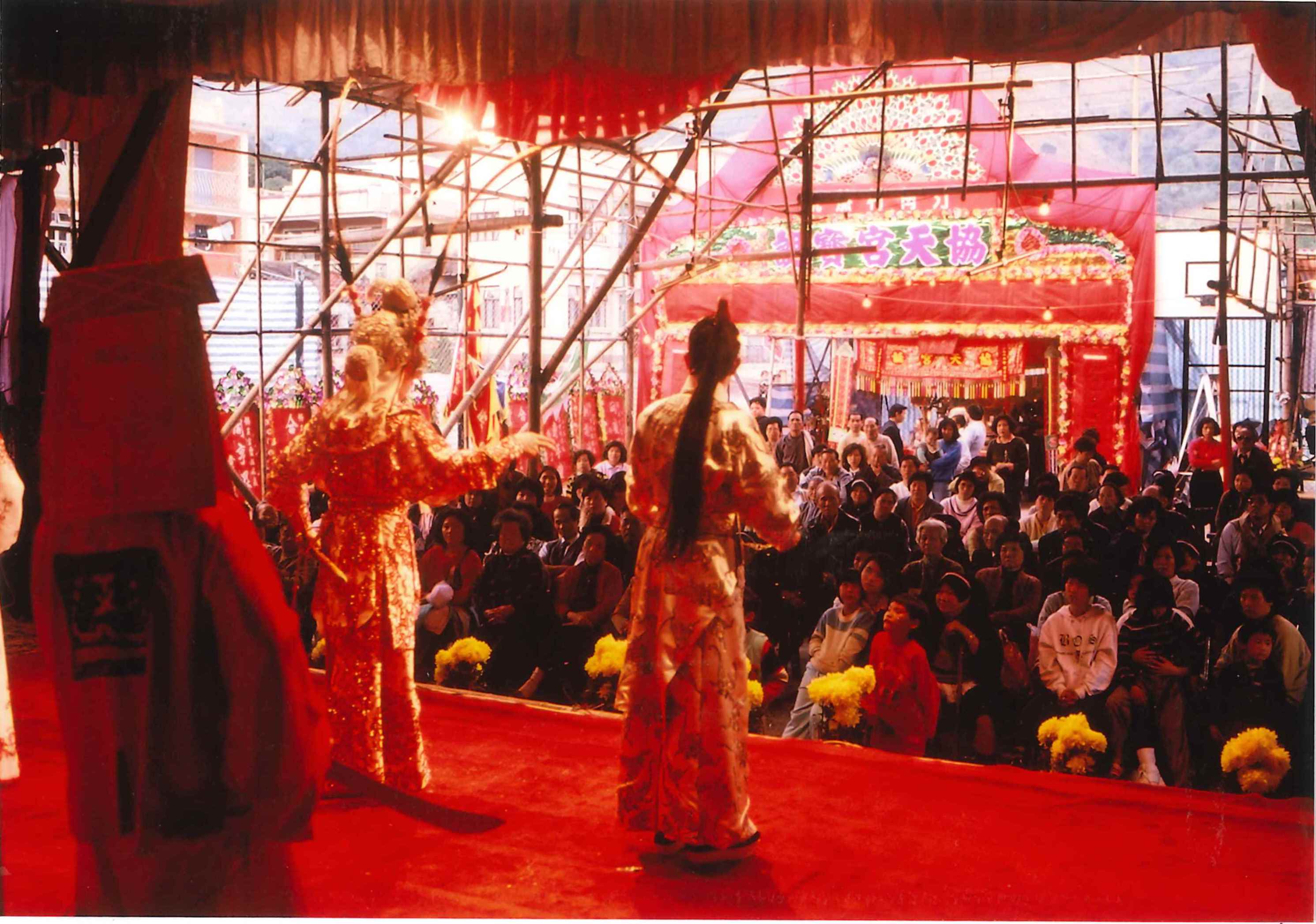 從後台外望，舞台的布幕、地氈及台下的裝飾多以紅色為主調，象徵快樂的氣氛。（汀角村；關帝誕；1990）
